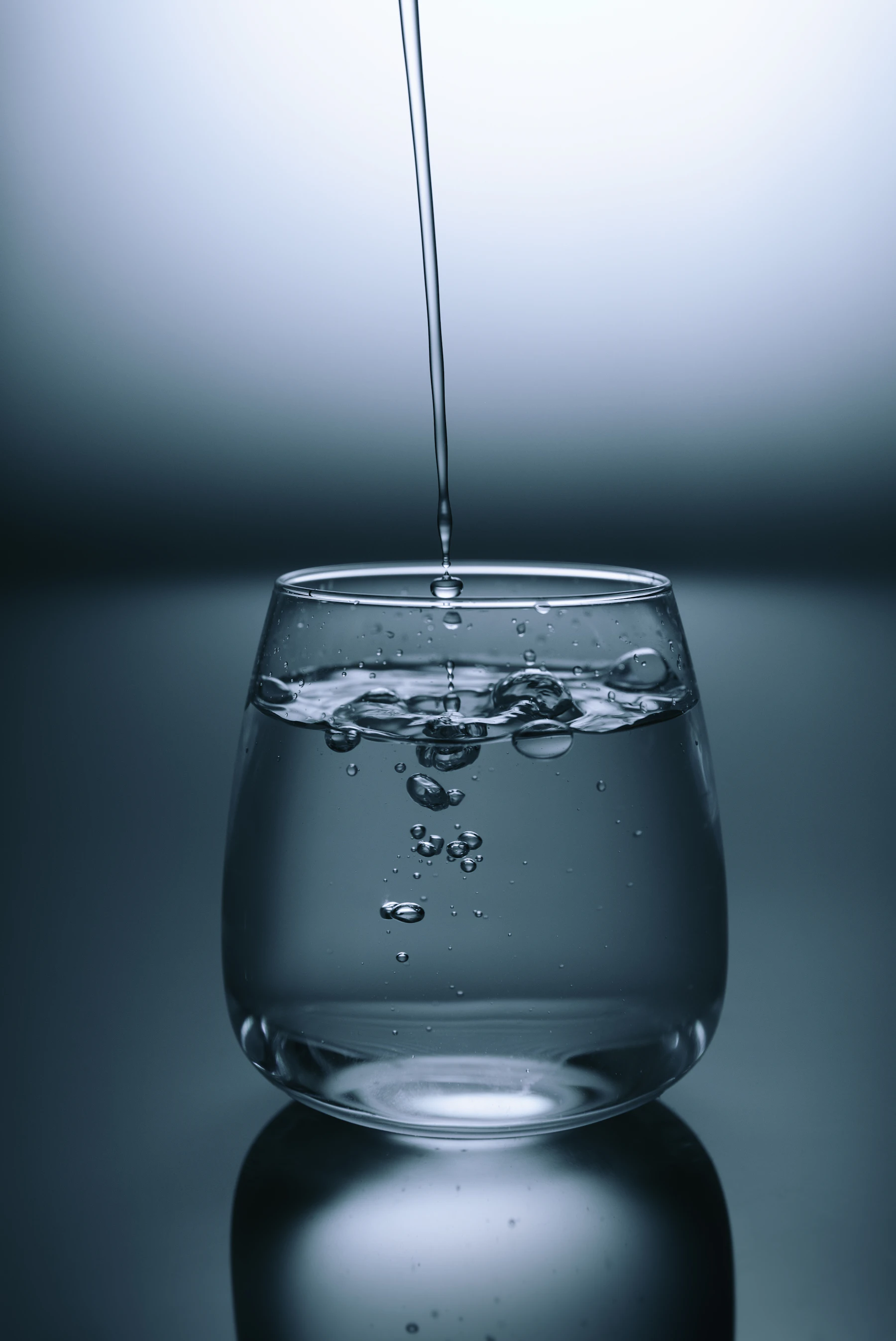 A clear glass of water with droplets on a grey surface