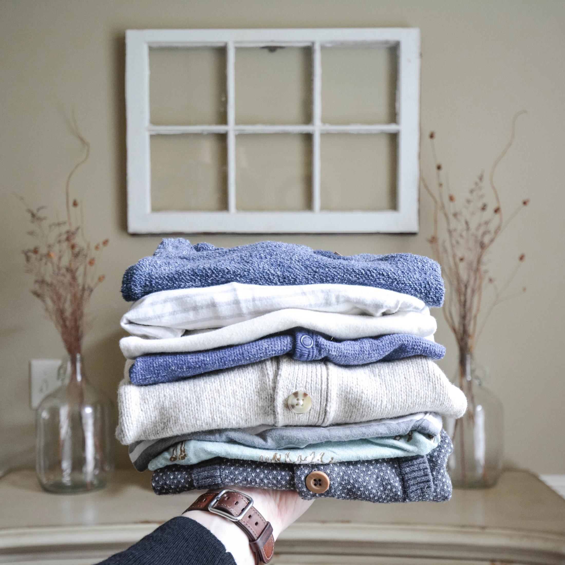 A hand holding a folded stack of sweaters and shirts